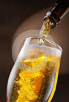 Jet of beer out of the bottle is poured into a beer glass, causing a lot of bubbles and foam