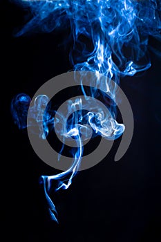 Jet of blue smoke isolated on black background. Chaotic curls of cigarette smoke, vertical pattern