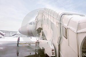 Jet bridge and white airplane parked on airport ground with airline staff