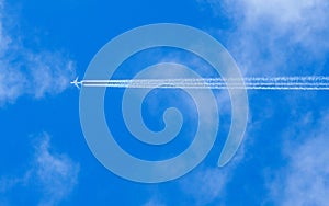 A jet flies across a blue cloudy sky leaving vapour trails