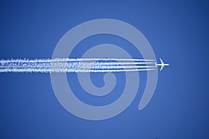 A jet plane flying overhead leaves four condensation trails against a vivid, blue sky.