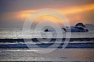 Jet ski and leisure boat parked on the sea in a reddish sunset with cloudy sky