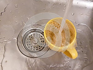 A jet of water filling a yellow mug with water in an iron gray sink