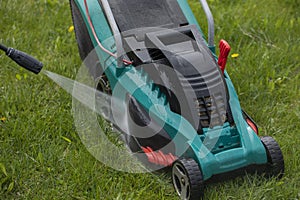 Jet of water from high-pressure washer cleans lawn mower on green grass