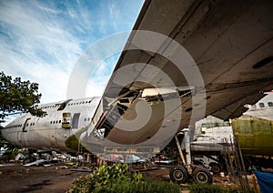 Jetliner Being Cut To Pieces For Recyling Purpose at Airplane Graveyard Under The Blue Cloudy Sky. Under Wing Part Being Dismantle