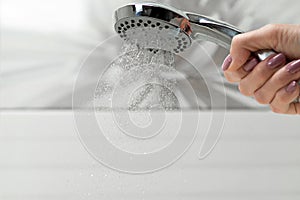 Jets of water flow from the shower head in the female hand.