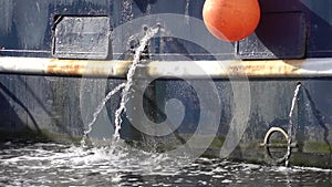 Jets of water from the holes in the blue Board of a metal fishing ship. Marine engine cooling system