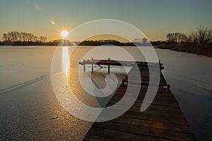 Jetty on a frozen lake, sunshine glow on the sky, winter view