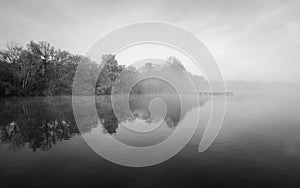 Jetty at the lake in the fog. Misty landscape in the morning. Idyllic nature by the water.