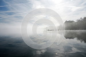 Jetty at the lake in the fog. Misty landscape in the morning. Idyllic nature by the water.