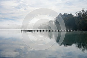 Jetty at the lake in the fog. Misty landscape in the morning. Idyllic nature by the water.