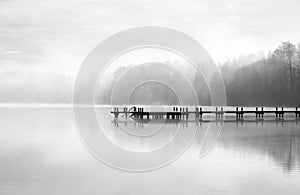 Jetty at the lake in the fog. Misty landscape in the morning. Idyllic nature by the water.
