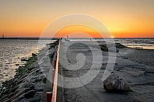 A jetty or pier with silhouetted people with a sunset at sea.