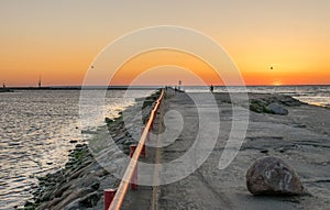 A jetty or pier with silhouetted people with a sunset at sea.