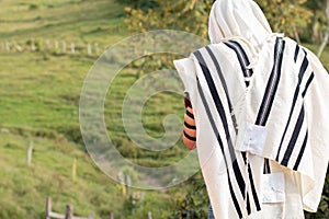 Jew wearing tallit and Tefillin or Phylactery praying outdoors against a background of nature. Jew covers his head with