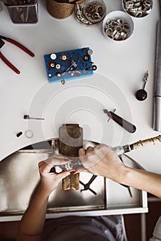 Jeweler`s workplace. Top view of jeweler`s workbenche with different tools on a white table. Female hands making a new