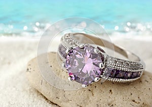 Jewelery ring with violet gemstone on sand beach with copy space