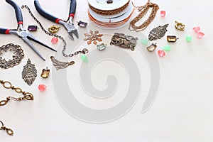 Jewellery making concept with brass chain, filigree charms, jems and tools over white wooden background photo