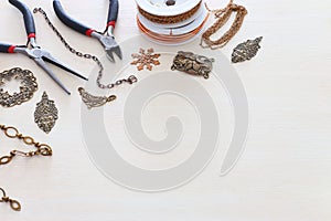 Jewellery making concept with brass chain, filigree charms and tools over white wooden background