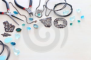 Jewellery making concept with cooper chain, filigree charms, jems and tools over white wooden background photo
