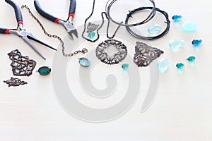 Jewellery making concept with cooper chain, filigree charms, jems and tools over white wooden background photo