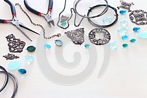 Jewellery making concept with cooper chain, filigree charms, jems and tools over white wooden background photo