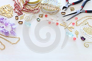 Jewellery making concept with gold chain, filigree charms, pearls, jems and tools over white wooden background photo