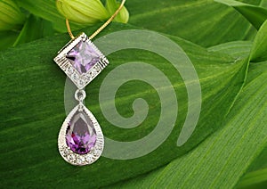 Jewellery pendant with diamonds and spinel on green leafs background, copyspace