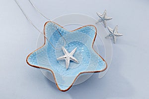 Jewellery set of starfish shape silver pendant necklace and earrings on blue background