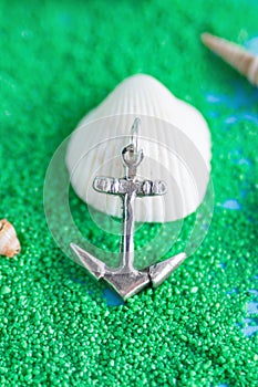 Jewelry anchor pendant from silver with seashells on an artificial green sand. Handcraft precious item.