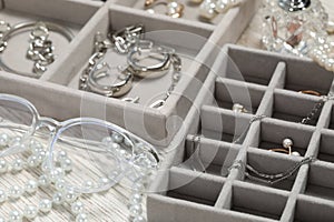 Jewelry boxes with many different accessories and glasses on white wooden table, closeup