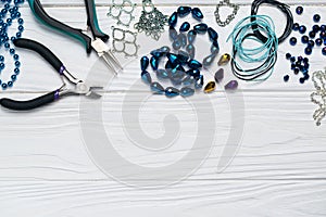 Jewelry findings handmade craft composition with pliers beads embellishments on white wooden background