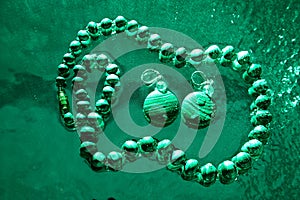 Jewelry from green malachite. Malachite beads in the studio on a glass surface with water