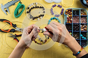 Jewelry making. Female hands with a tool on a yellow background