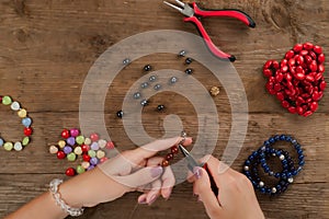 Jewelry making. Making a bracelet of colorful beads. Female hands with a tool on a rough wooden table.