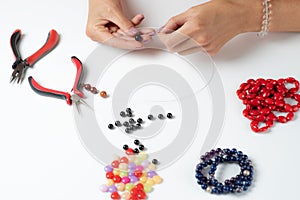 Jewelry making. Making a bracelet of colorful beads. Female hands with a tool on a white background.