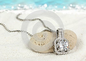 Jewelry pendant with big diamond on sand beach as background photo