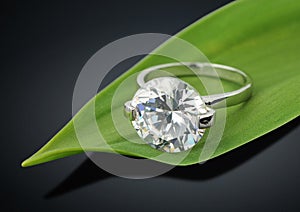 Jewelry ring with big diamond on green leafs background