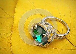 Jewelry ring with gemstone on yellow leaves background, copy sp