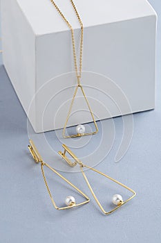 Jewelry set of triangle shape gold earrings and pendant necklace with pearls on gray background