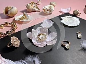 Jewelry white pearl gold rings on a black background with pink opal in seashell , precious stones, rose petals and feathers concep