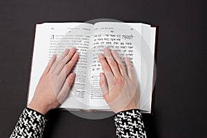 Jewish book, with woman`s hand, on black background. Text of the Hebrew, prayer. Woman prays with book.