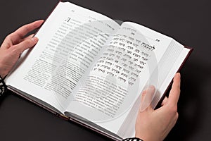 Jewish book, with woman`s hand, on black background. Text of the Hebrew, prayer. Woman reading book.