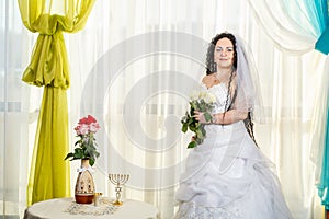 A Jewish bride in a synagogue before a chuppa ceremony during a pandemic, wearing a medical mask and a bouquet of