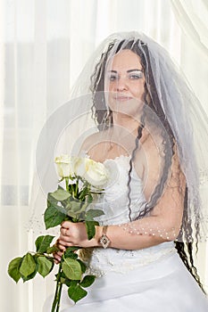 Jewish bride with a veiled face covered before a chuppa ceremony with a bouquet of white roses in her hands.