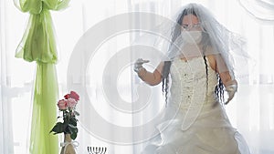 A Jewish bride in a wedding dress and a veil wearing a medical mask covers her head with a veil before the wedding