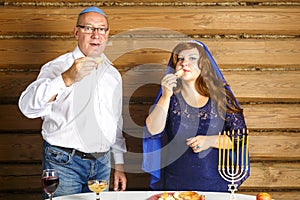 A Jewish family, a husband in a kippah and a wife in a cape on their heads in Rosh Ashana eat challah in honey at a