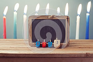 Jewish Holiday Hanukkah background with wooden dreidel spinning top and chalkboard over candles