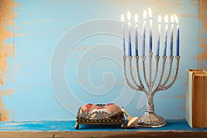 Jewish holiday Hanukkah concept with menorah, sufganiyah and book on vintage background