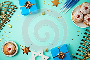 Jewish holiday Hanukkah concept with menorah, sufganiyah, gift box and spinning top over blue background